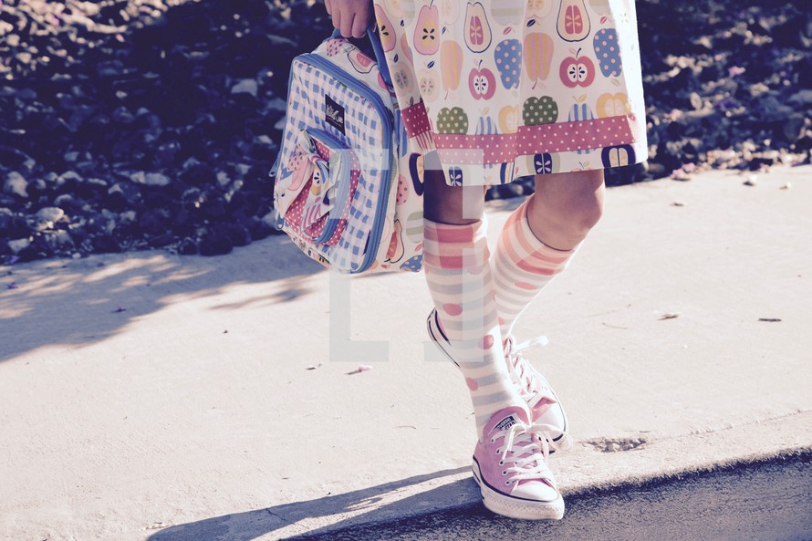 legs of a little girl carrying a lunch box and wearing knee socks 