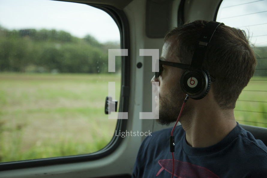 man listening to headphones and looking out a car window 