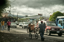 man pushing a cart along the side of a road 