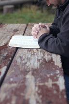 man praying near and open Bible on a picnic table 