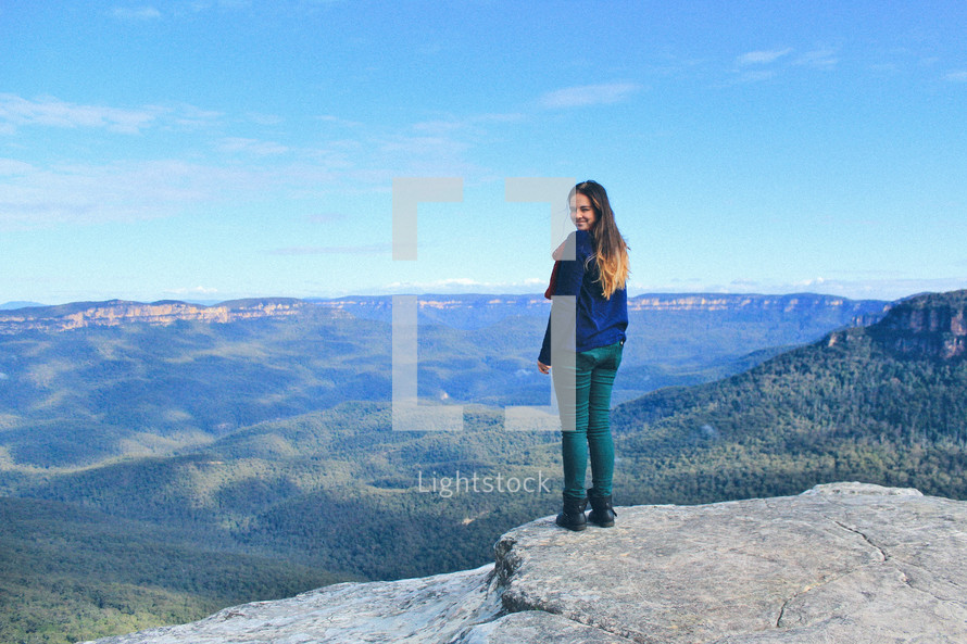 woman standing on the edge of a cliff on top of a mountain 
