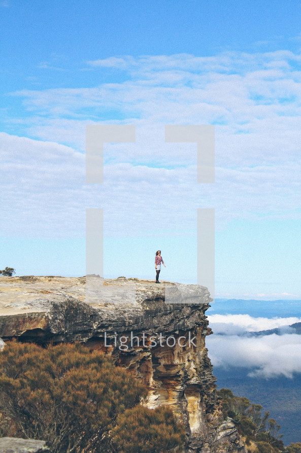 woman standing on the edge of a cliff on top of a mountain 