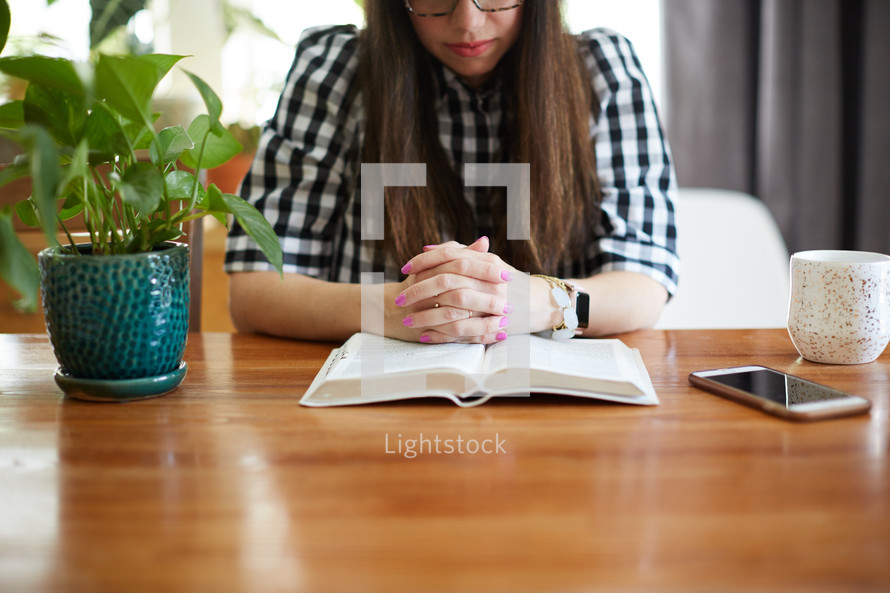 a woman sitting at a table praying over a Bible 
