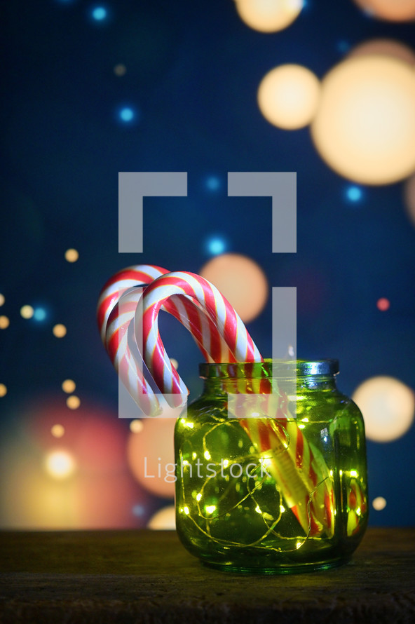 Candy canes and twinkle lights in a green jar with whimsical background