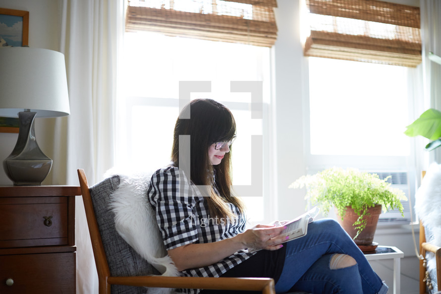a woman sitting in a chair reading a Bible at home 
