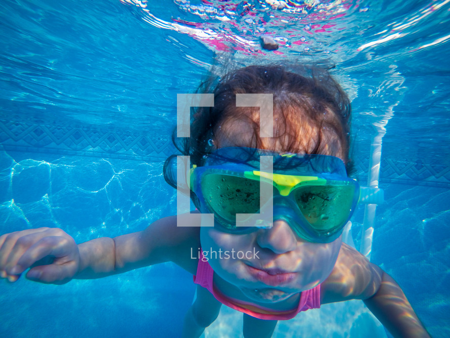 little girl with goggles under water swimming 