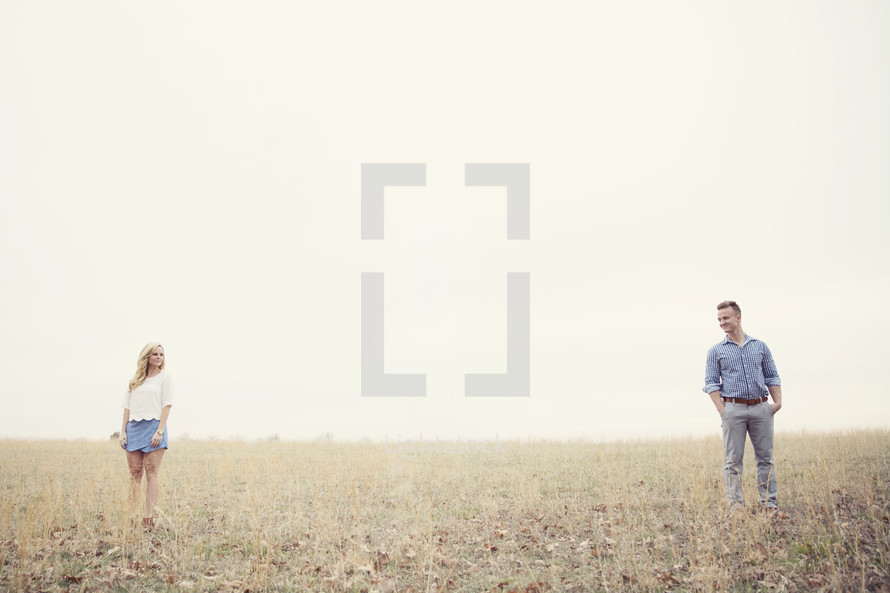 A man and woman stand far apart in a field of grass.