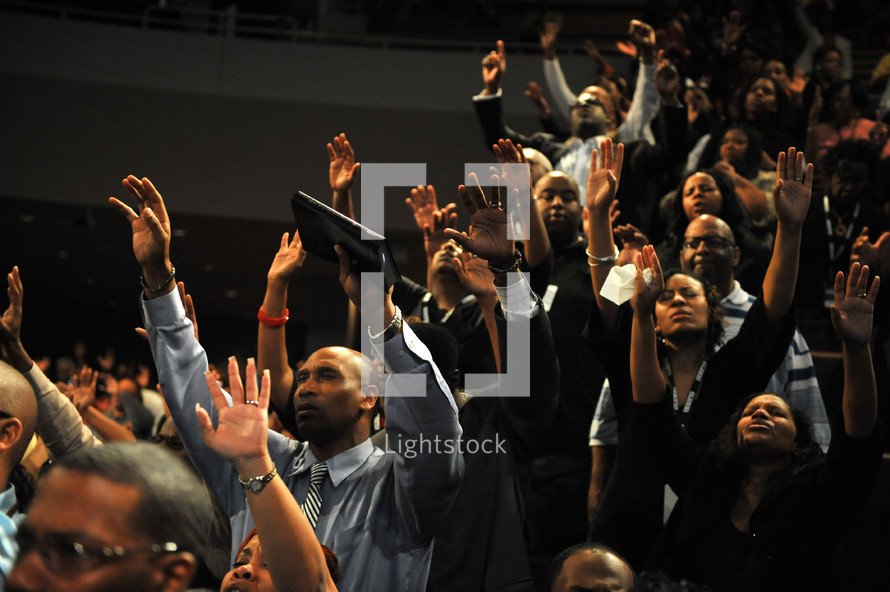 Congregation with arms raised praising God during worship service.