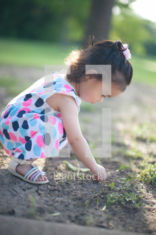 Girl squatting in a field outside.