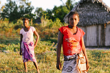 young girls standing in front of a hut 