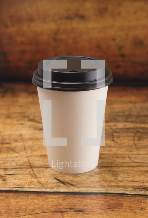 Disposable White Coffee Cup with Black Lid on a Wood Background