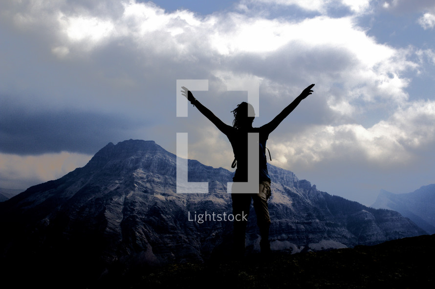 silhouette of a woman with raised arms on a mountain 