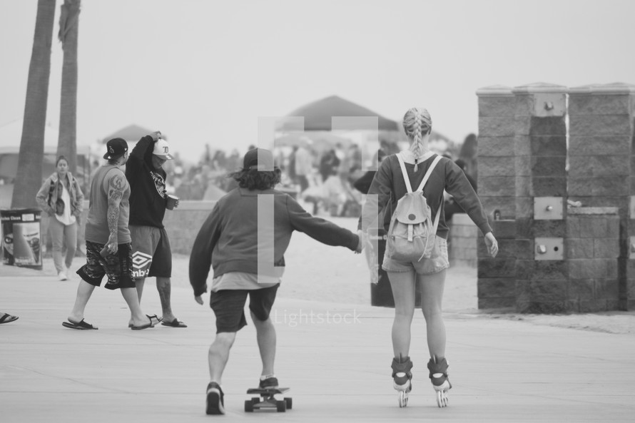 a couple holding hands skateboarding and roller blading on a boardwalk 
