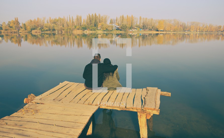 a couple sitting at the end of a dock 