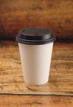 Disposable White Coffee Cup with Black Lid on a Wood Background