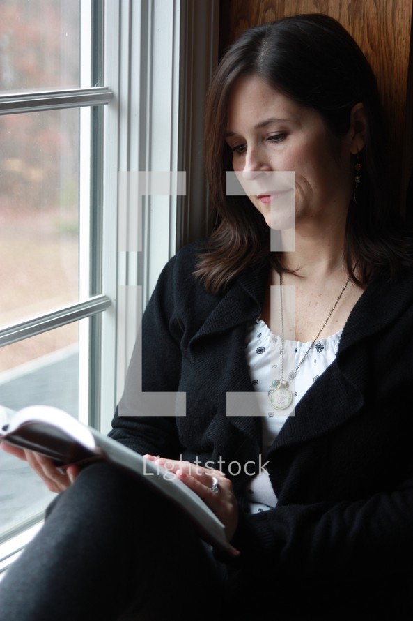 a woman sitting in a window reading a Bible 