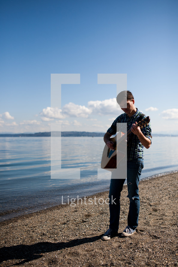 man playing a guitar by a lake
