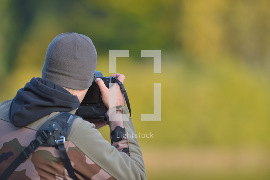 Wildlife photographer in camouflage outfit shooting, taking pictures