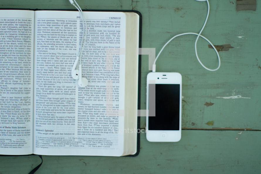 Iphone and earbuds on a wooden table with an open Bible.
