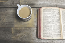 coffee mug and pages of an opened Bible 
