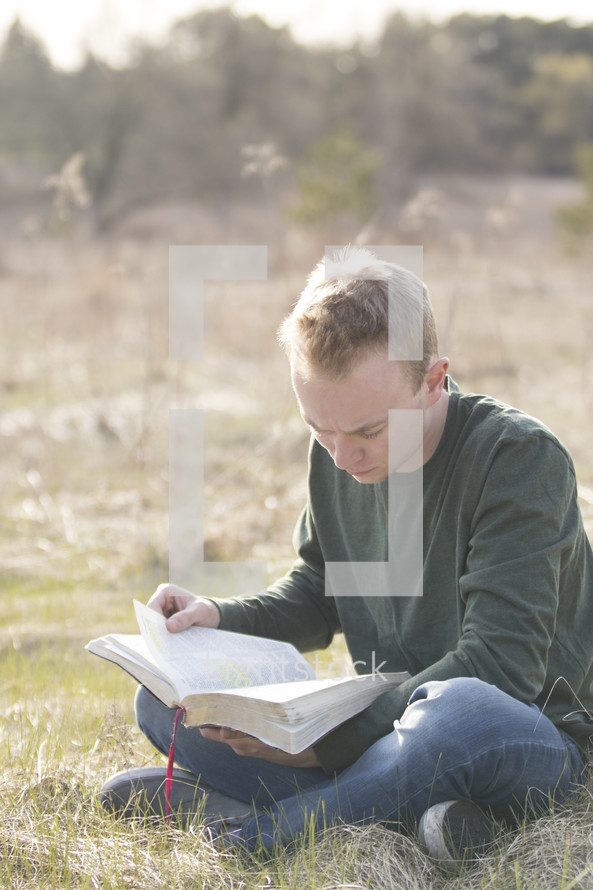 a man sitting in a field reading a Bible 