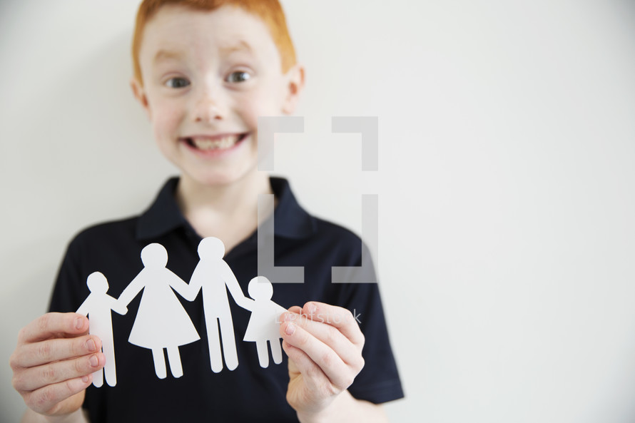 A smiling boy holding a paper cut-out of a family.