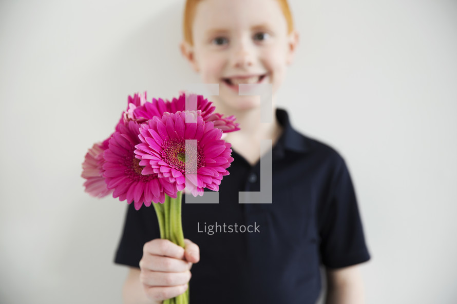 A boy holding out a handful of bright pink flowers.