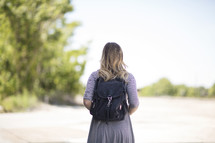 a woman with a book bag standing with back to the camera 