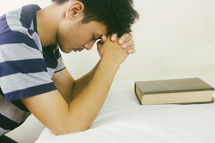 man kneeling at his bedside praying 