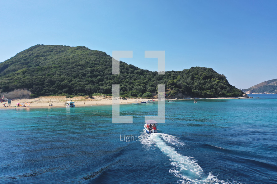 Small boat with tourists heading to iconic small uninhabited island of Marathonisi featuring clear water sandy shore and natural hatchery of Caretta-Caretta sea turtles, Zakynthos island, Ionian, Greece