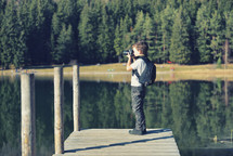 Creative child, kid photographer (a little boy) with a camera taking landscape pictures near la lake