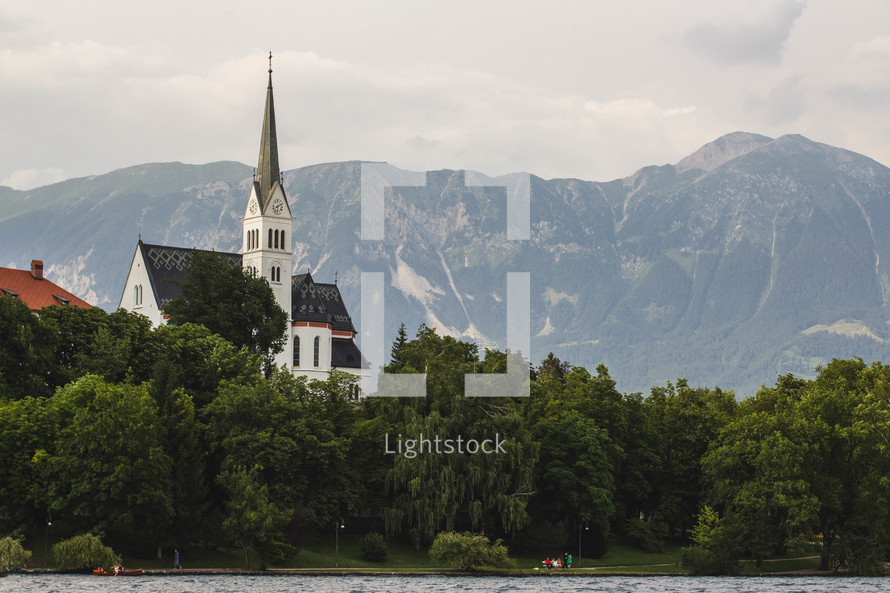 A church with a tall steeple surrounded by mountains and a lake.