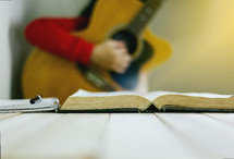 a woman playing a guitar and reading a Bible 