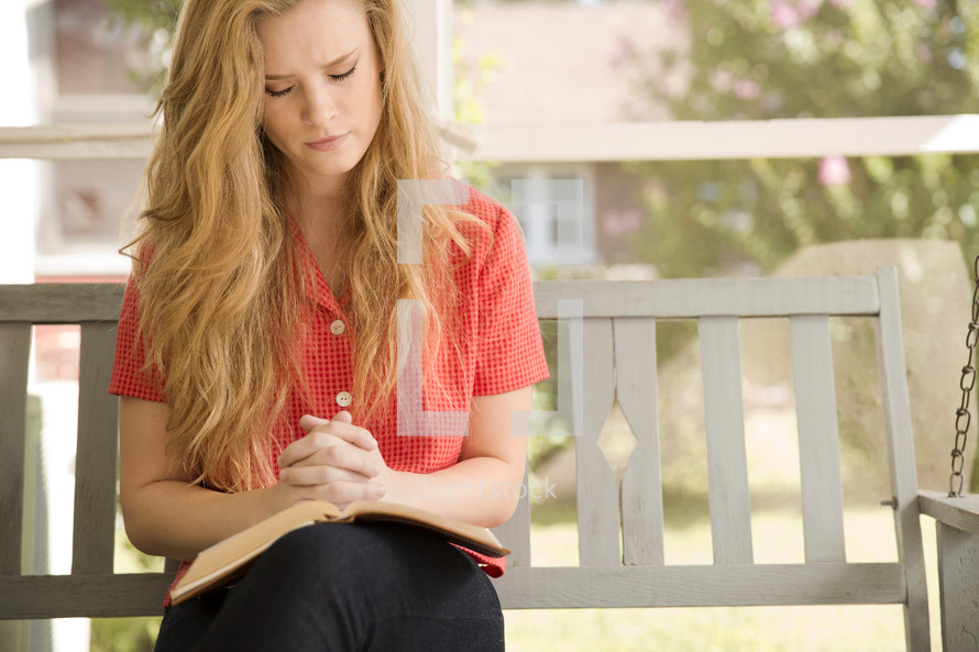 woman sitting on a porch swing praying with a Bible in her lap 