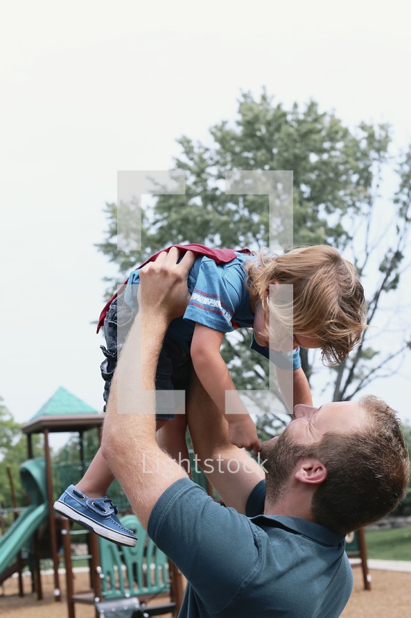 a father holding his son in the air at a playground 