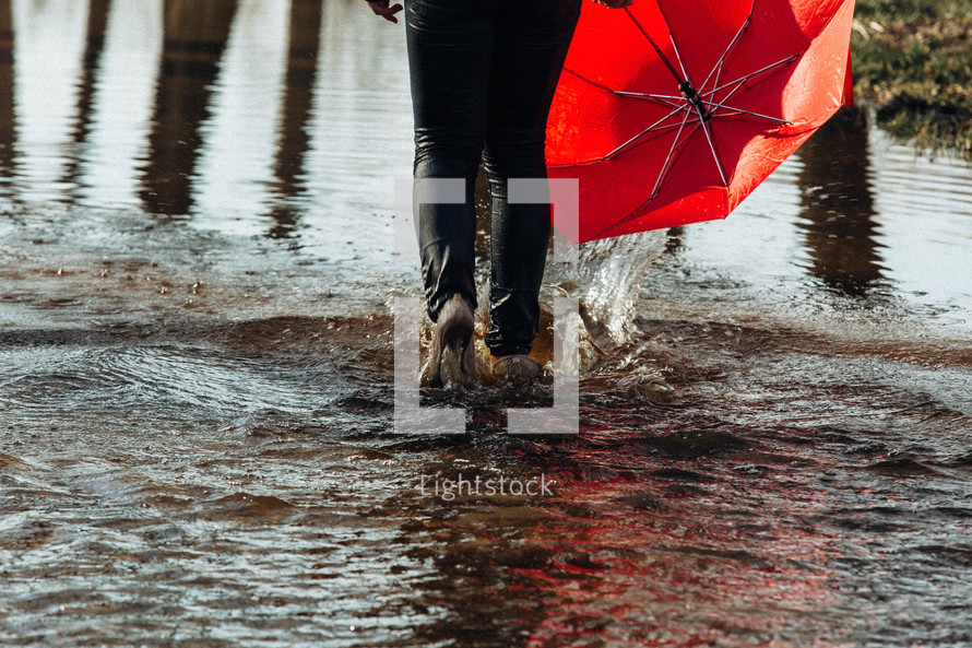 woman walking through a puddle carrying an umbrella 