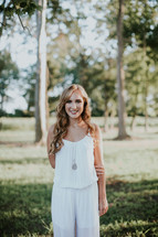 young woman in a white romper posing outdoors in a park 