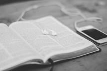 Iphone on a wooden table with earbuds on an open bible.