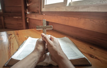 hands holding a wooden cross over a Bible 