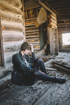 A woman sitting with hand on head in an abandoned log house.