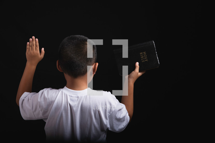 Boy praising to God with hands raised and a Bible