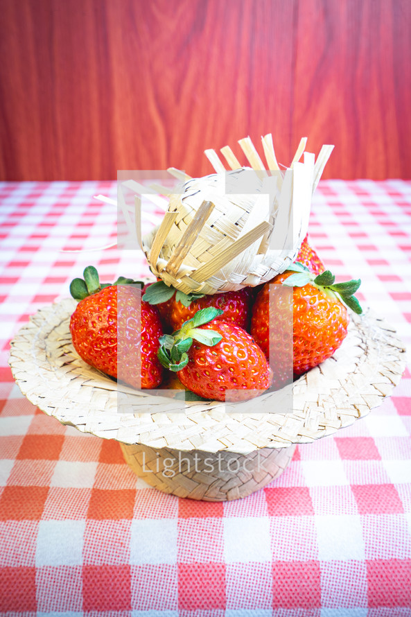 Fresh strawberries decorated on a straw hat. on a red picnic blanket.