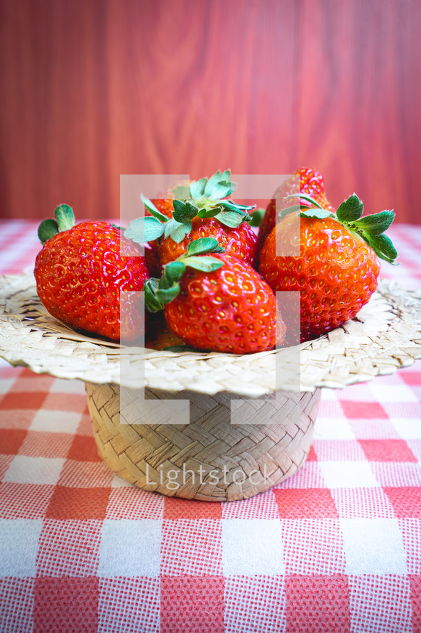 Fresh strawberries decorated on a straw hat. on a red picnic blanket.