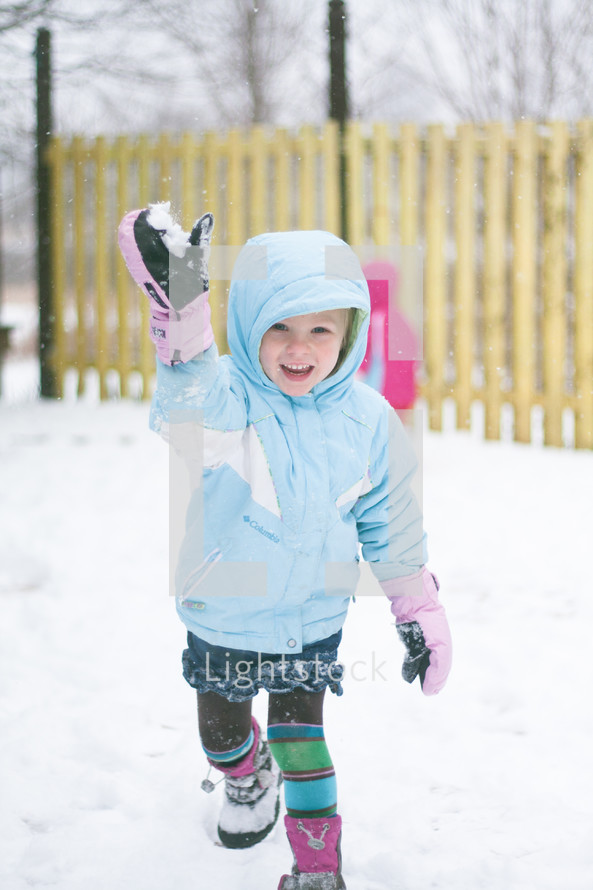 a girl child in mittens playing in the snow 
