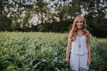young woman in a white romper standing in a field of crops 