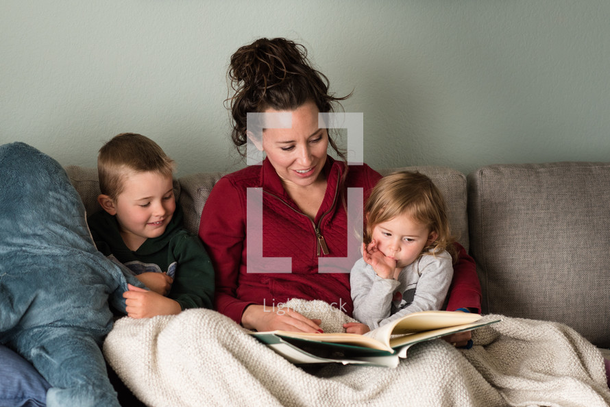 a mother reading a book to her children on the couch 