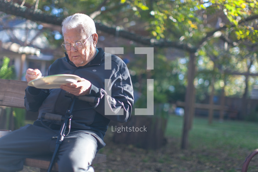 an elderly man eating on a bench outdoors 