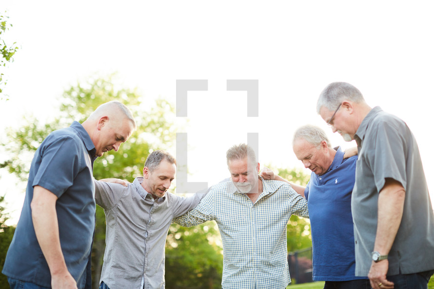 men standing in a backyard praying together 
