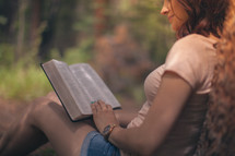 woman sitting outdoors reading a Bible by a tree