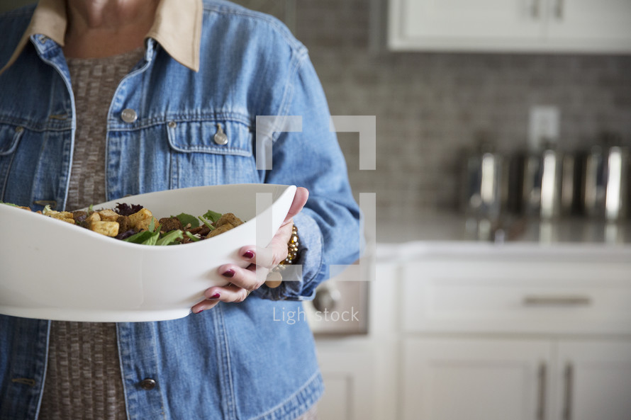 a woman holding a large bowl of salad 